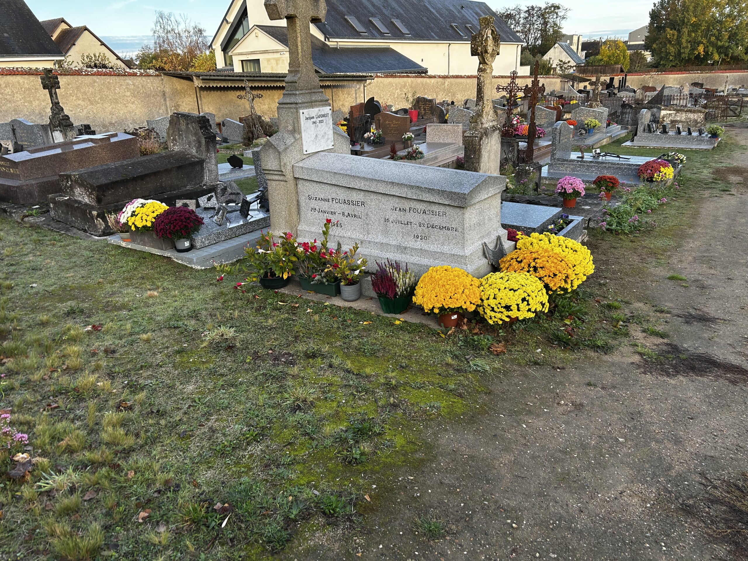 Tombes anciennes et récentes réunies dans un cimetière, avec croix de pierre et bouquets de chrysanthèmes jaunes et roses.