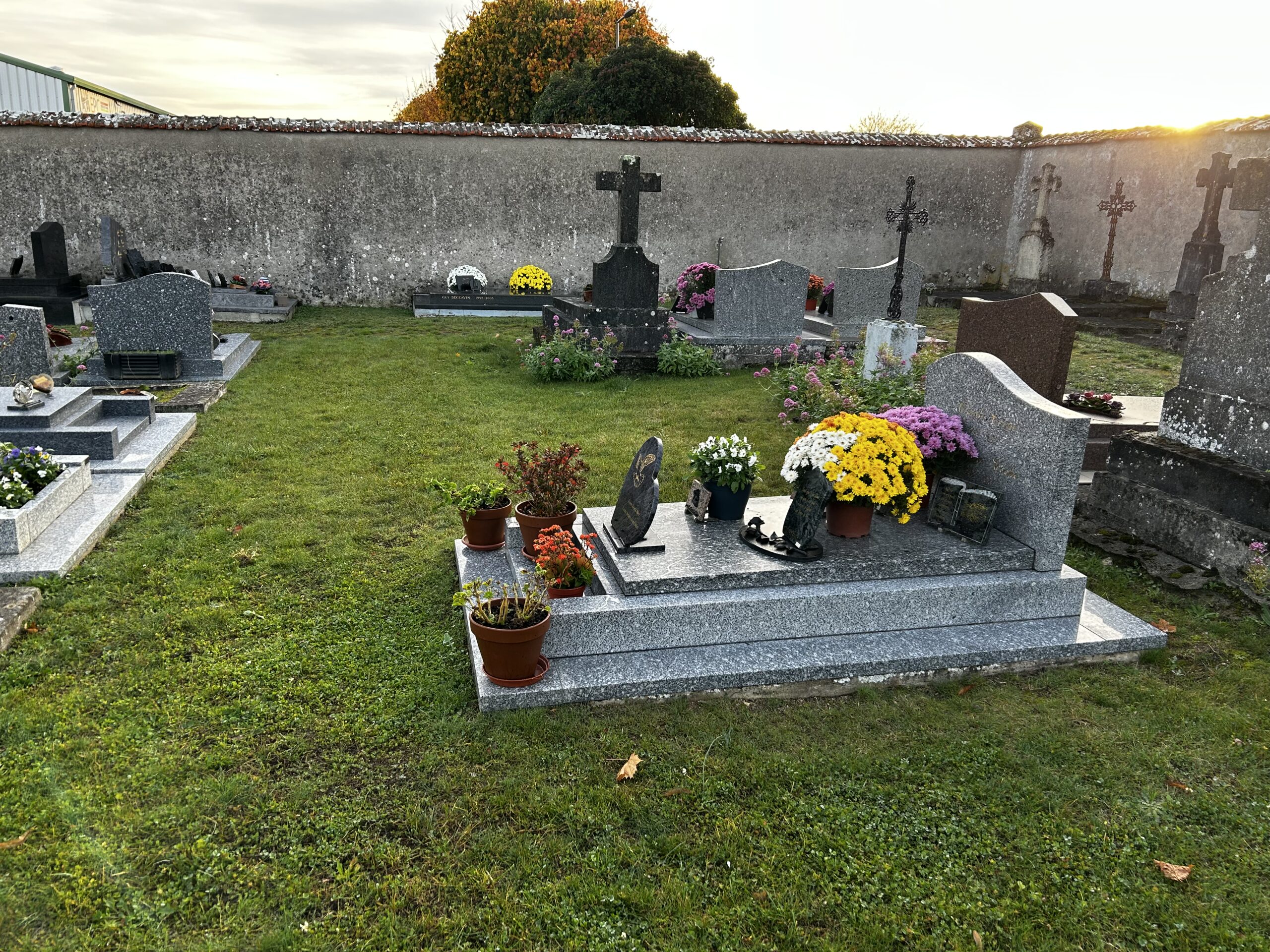 Vue d'un cimetière à la lumière du soir, avec des tombes fleuries de chrysanthèmes et plusieurs croix de pierre.