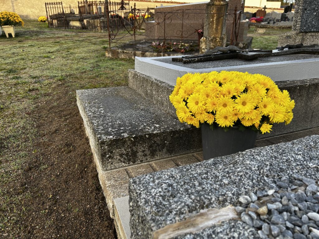 Monuments funéraires de différentes époques entourés de fleurs d'automne et de chrysanthèmes jaunes dans un cimetière.