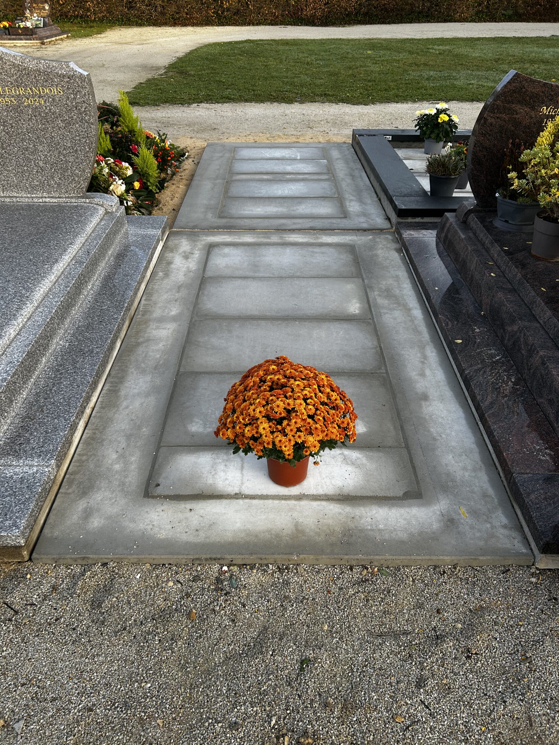 de chrysanthèmes orange posé au centre d'une tombe grise, entre deux monuments funéraires.